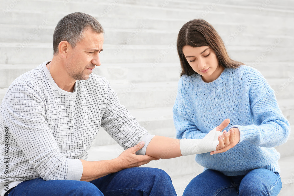 Young woman applying bandage on mature man's arm outdoors Young woman applying bandage on mature man's arm outdoors