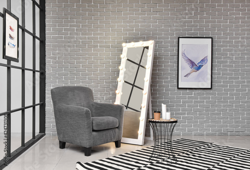 Interior of modern room with comfortable armchair, mirror and table photo