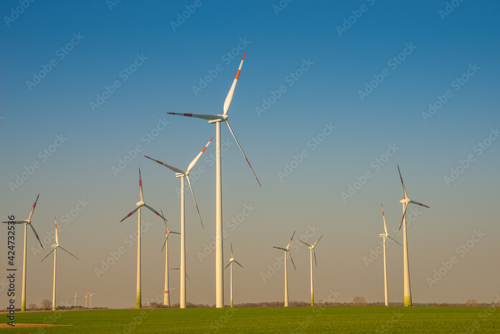 Group of big wind turbines to generate electrical power, green ecofriendly energy at blue sky with sunset warm colors in Europe. Concept of green sustainable energy production. Group of big wind turbines to generate electrical power, green ecofriendly energy at blue sky with sunset warm colors in Europe. Concept of green sustainable energy production.