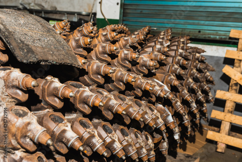 Close-up of heavy tools for lifting asphalt. Tungsten carbide burs placed along the cylinder. Workshop cabinet in the background. Road repair concept. Horizontal plane.