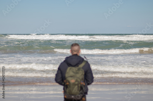 Chico de espaldas con una mochila verde mirando la playa