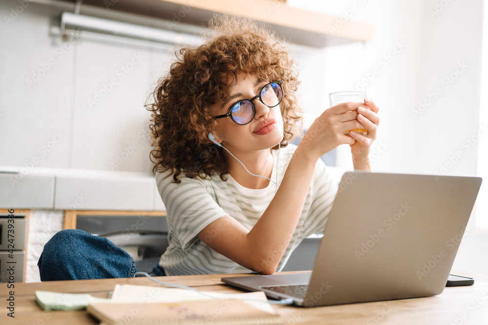 European thinking woman using laptop and earphones while drinking juice European thinking woman using laptop and earphones while drinking juice