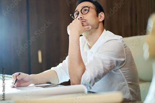 Photography Asian bearded designer sitting, thinking and sketching ideas indoors