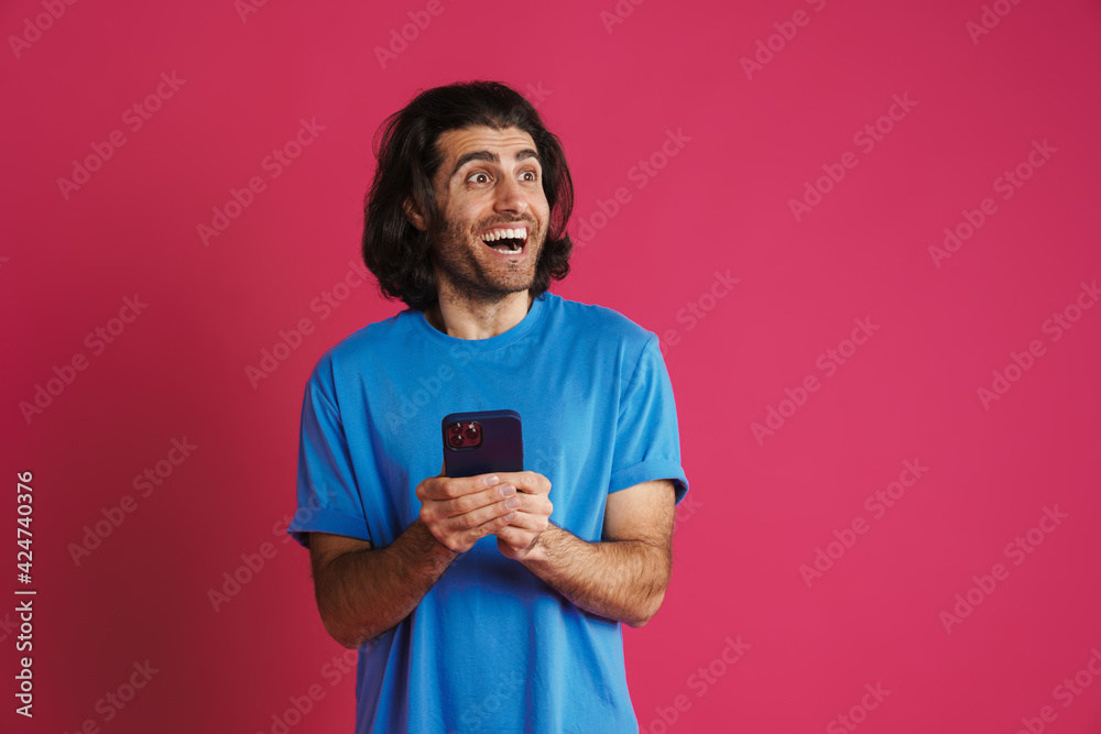 Excited brunette man in t-shirt using mobile phone and smiling Excited brunette man in t-shirt using mobile phone and smiling