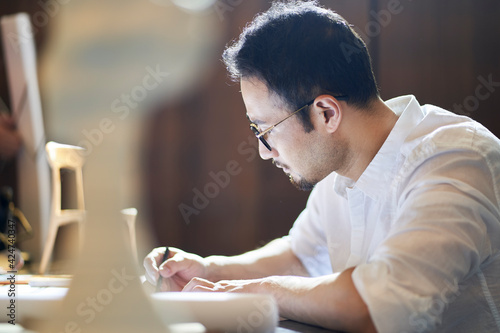 Asian bearded designer sitting, thinking and sketching ideas indoors