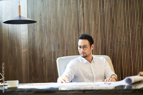 Photography Asian bearded designer sitting, thinking and sketching ideas indoors