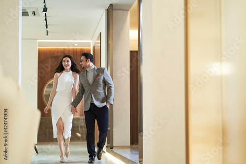 Asian happy upscale couple walking in hallway hand in hand smiling