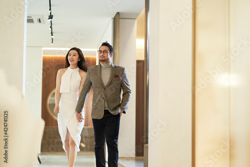 Asian happy upscale couple walking in hallway hand in hand smiling