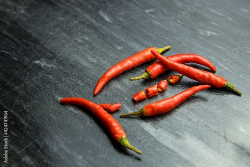 Red chilli peppers and one sliced chilli pepper on black background