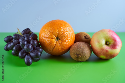 Ripe blue grapes, orange, kiwi and apple on a gray green background