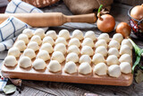 Homemade dumplings of their dough and minced meat, a set of products for cooking: flour, dough, minced meat, eggs, olive oil, spices, salt, pepper, bay leaf on a wooden board.