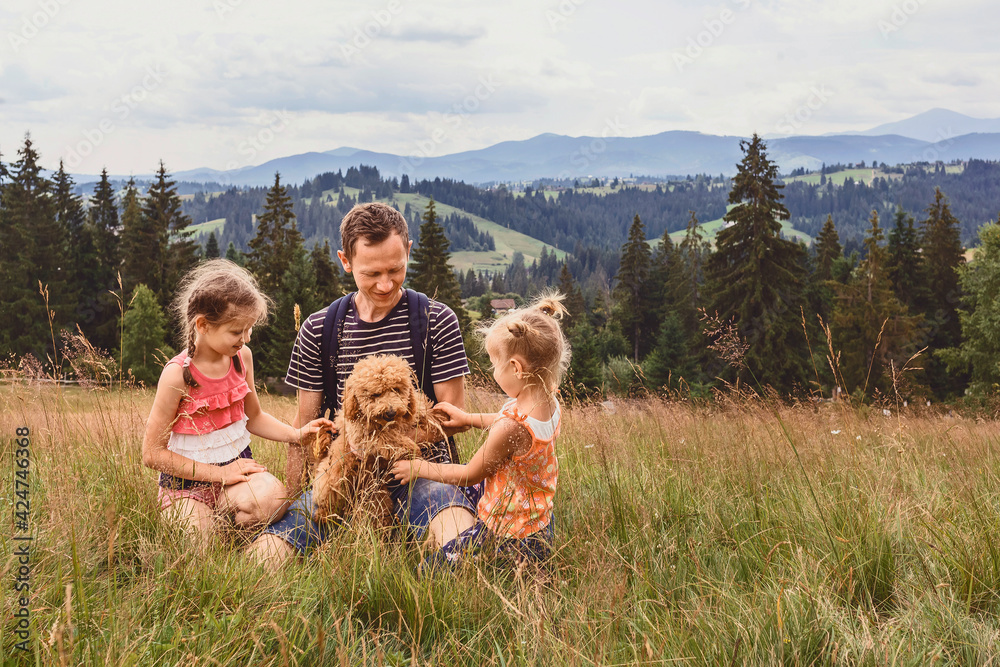 Dad with two little daughters and a dog on a glade on a background of mountains. Family with a little dog on a hike Dad with two little daughters and a dog on a glade on a background of mountains. Family with a little dog on a hike