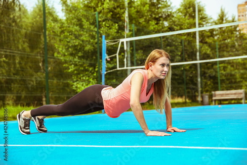young woman is doing sport exercises on sport ground outdoors in summer