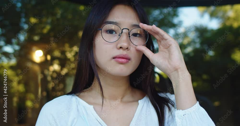 Portrait of attractive Asian businesswoman looking at camera and putting of glasses. Adult female lady worker standing in urban city street. Occupation, work concept. Park background. Portrait of attractive Asian businesswoman looking at camera and putting of glasses. Adult female lady worker standing in urban city street. Occupation, work concept. Park background.
