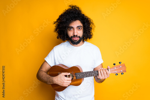 Sad african american guy with afro hairstyle and beard holds a ukulele in his hands and plays on it