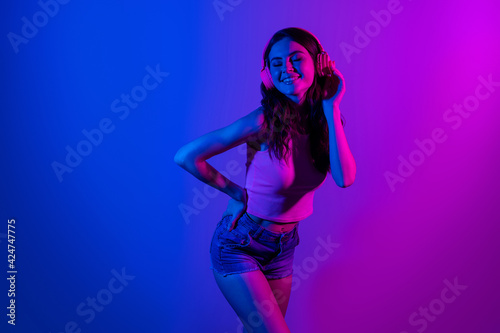 Photo of happy cheerful smiling beautiful girl dancing in headphones enjoying party disco isolated on glowing blue color background