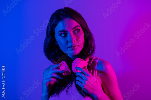 Photo of happy positive beautiful young woman with headphones look copyspace dreaming isolated on glowing background