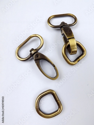 Haberdashery accessories, metal snap hooks or metal swivel clip snap hooks and D rings for bag strap, all in brass color. Isolated against white background. 