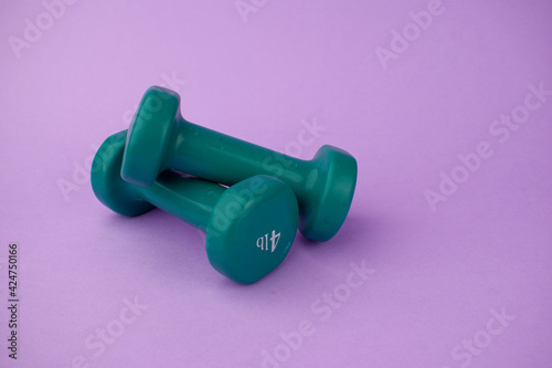 two green dumbbells stacked together on a purple background. Sports at home remotely. Home fitness and exercise concept.