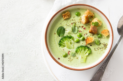 Summer cream soup with green fresh pea shoots. Top view. Green vegetable cream soup in a white bowl on a gray concrete background top view. Vegan soup puree of green vegetables. Vegetarian and diet fo