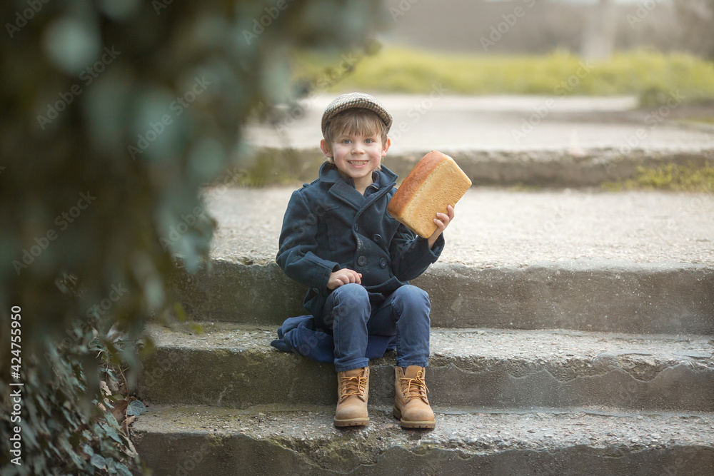 Beautiful little Caucasian boy with blonde hair holding a large loaf of bread. Funny happy baby bites and eats healthy bread outdoors. A hungry child. Beautiful little Caucasian boy with blonde hair holding a large loaf of bread. Funny happy baby bites and eats healthy bread outdoors. A hungry child.