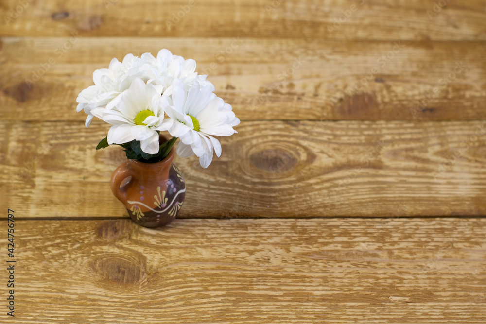 Small white fresh daisies in a brown clay vase on a light wooden background close-up Small white fresh daisies in a brown clay vase on a light wooden background close-up
