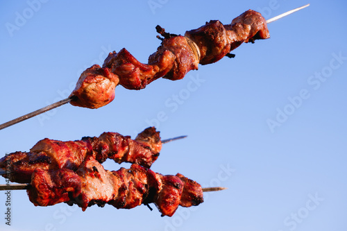 Juicy meat on skewers against the blue sky. Kebab of meat is fried on the grill.