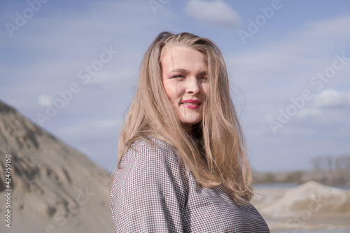 Beauty portrait of a young blond girl in a vintage dress. She is posing on a sandy landscape with harsh sun.