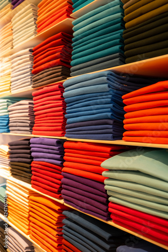 Vertical photo of clothes folded in a shelve and sorted by colour ranges