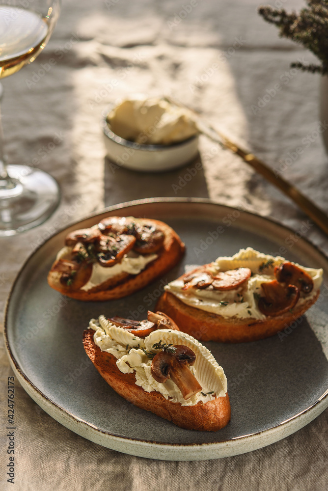 Bruschettas or toasts with cheese and fried mushrooms with thyme served with glasses of wine on greige linen tablecloth