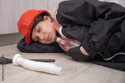 Foto a drunken plumber in uniform and hard hat sleeps on the floor, with tools and an empty bottle scattered nearby