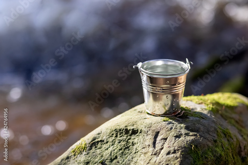 Aluminum bucket with water on the river bank. Water protection concept. Close-up. Place for your text.