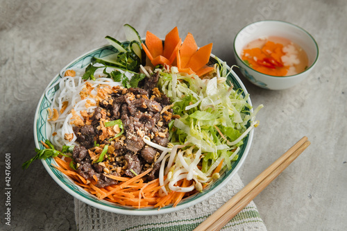 Photos A large bowl of traditional South Vietnamese noodle dish called Bun Bo Nam Bo with beef, noodles, fresh herbs, pickled vegetables and fish sauce