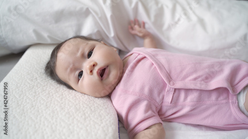 asian baby infant laying down on white soft bed feeling hungry. 3 months old baby facial expression. sign and symptom of hungry in kid.