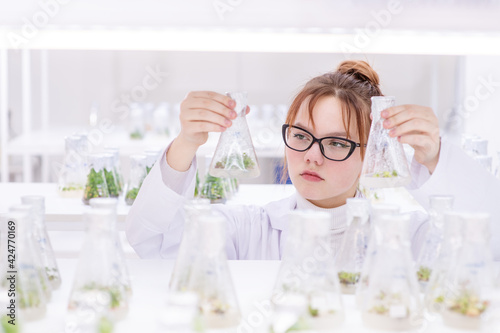 A girl laboratory assistant in a biological laboratory talking on the phone examining plants grown in a nutrient solution in flasks. Biological research at the university