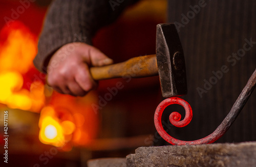 Close-up of the hands of a blacksmith twisting a spiral with a hammer, putting a red-hot iron blank on an anvil. Work in the forge photo