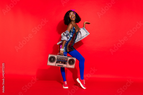 Photo of charming cute wavy dark skin lady wear pin up outfit holding boombox looking empty space isolated red color background