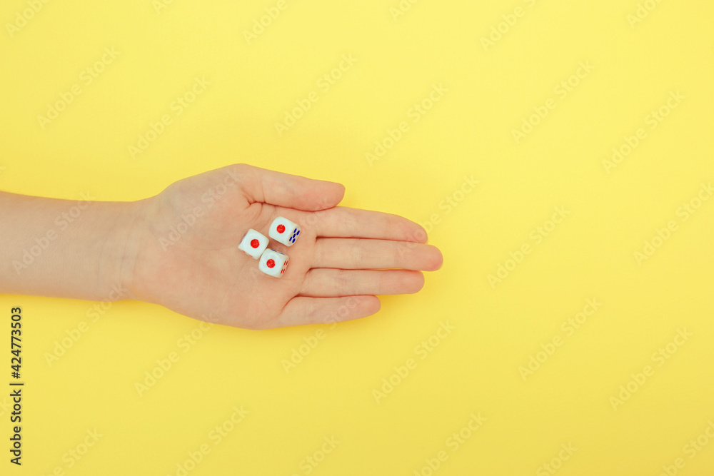 A woman's hand holds three dice. A game of dice with numbers. Board game items. yellow background.