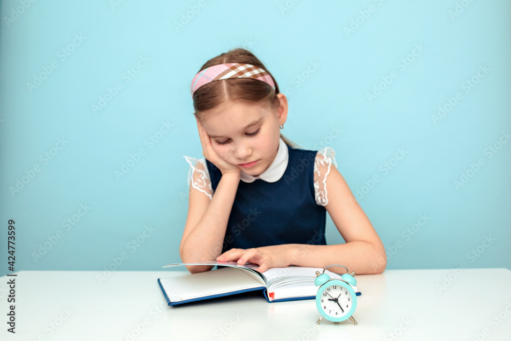 An angry and tired schoolgirl is studying with a book on the table. Education and distance learning for children. Home schooling during quarantine. An angry and tired schoolgirl is studying with a book on the table. Education and distance learning for children. Home schooling during quarantine.