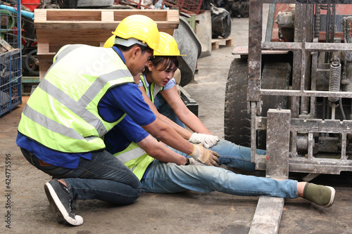 Accident at workplace, industrial engineer worker wearing helmet hit by forklift car at manufacturing plant factory construction site building, man leg stuck in forklift, colleague try to help him