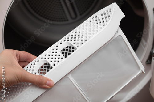 A woman's hand takes out the filter of the drying machine. Down filter for clothes dryers. Removing fluff from the dirty air filter of the dryer after using the machine. photo