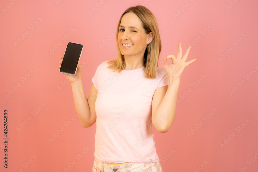 Beautiful young smiling woman showing mobile phone isolated over pink background. Beautiful young smiling woman showing mobile phone isolated over pink background.