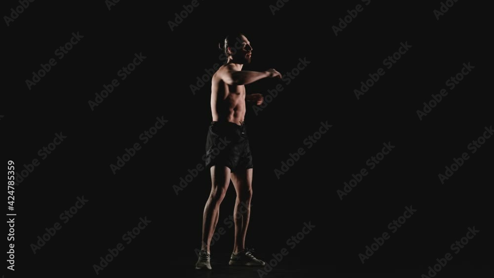 An athletic man does a warm-up on a black background. Slow motion An athletic man does a warm-up on a black background. Slow motion