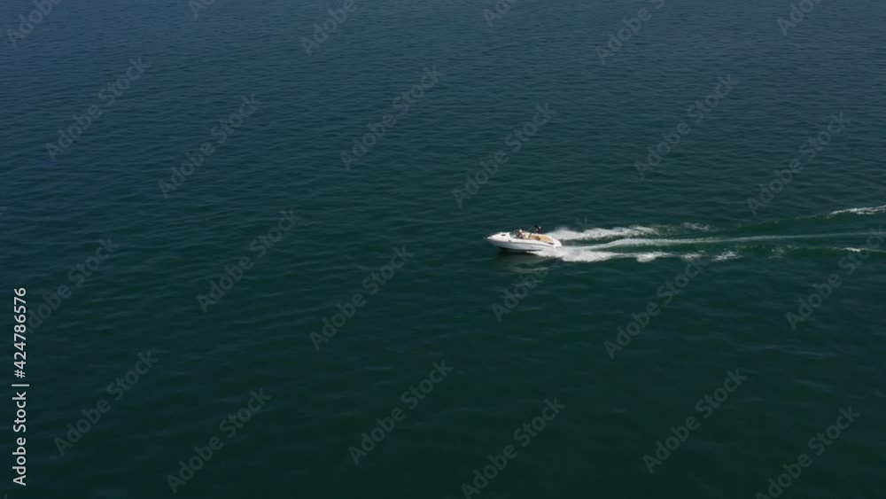 Boat in motion aerial view, drone shooting. White open boat high speed. A large white boat is moving quickly horizontally on dark blue water in the ocean.
