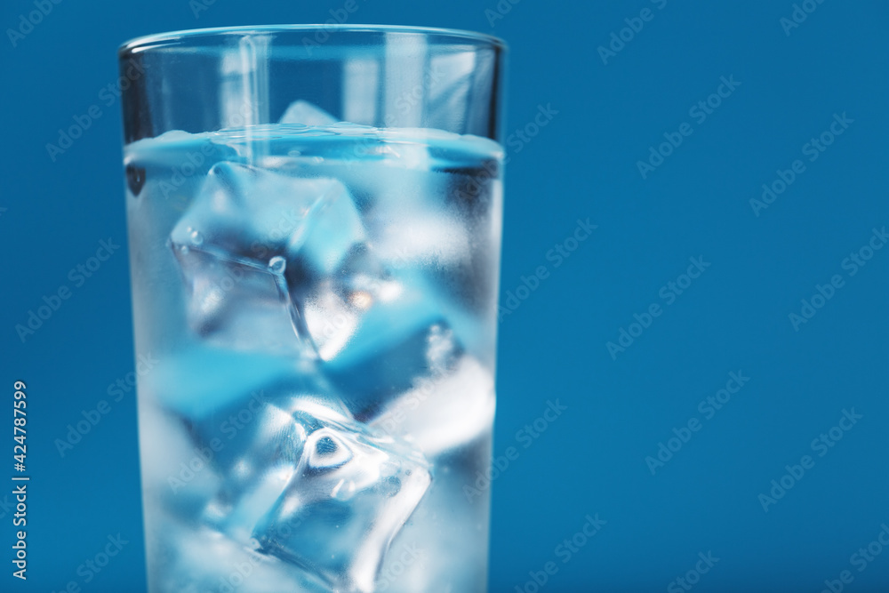 Ice cubes in a glass with crystal clear water on a blue background. Ice cubes in a glass with crystal clear water on a blue background.