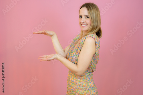 Young woman over isolated background holding something with both hands, product presentation. © Danko