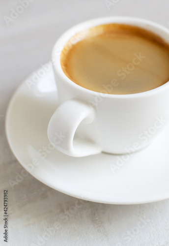 Fragrant espresso in a white cup and saucer. Morning of tradition. Homemade coffee making concept. Vertical orientation. Close-up.