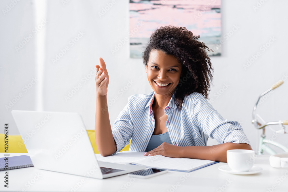 African american woman pointing at camera near gadgets and cup of coffee on blurred foreground at home African american woman pointing at camera near gadgets and cup of coffee on blurred foreground at home