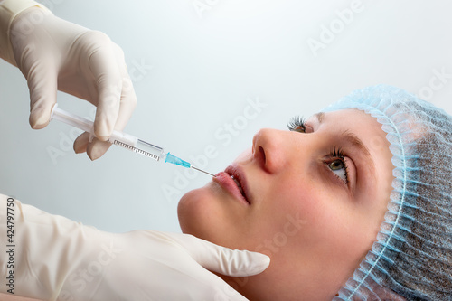 Cosmetic surgeon injecting botox to lower lip of a young woman.