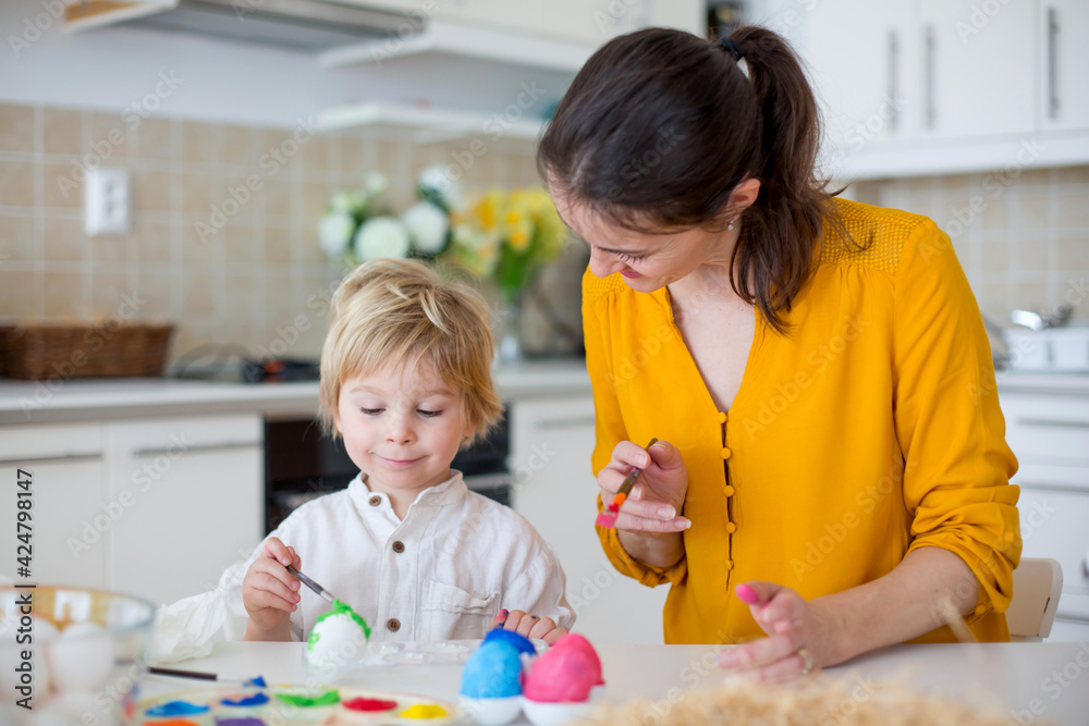 Beautiful blond child, toddler boy, painting easter eggs with mother at home, making easter wreath Beautiful blond child, toddler boy, painting easter eggs with mother at home, making easter wreath